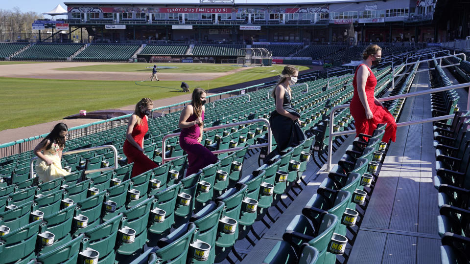 While wearing their prom gowns, students walk through the stands along the third baseline at the New Hampshire Fisher Cats minor league baseball stadium in Manchester, N.H., on Monday, April 26, 2021. After a year without proms, school districts across the country are debating whether they can safely hold an event that many seniors consider a capstone to their high school experience. The nearly 300 student senior class of Manchester's Central High School are waiting to get approval from the city's board of health so they can have their prom at the outdoor venue, due to COVID-19 concerns. (AP Photo/Charles Krupa)