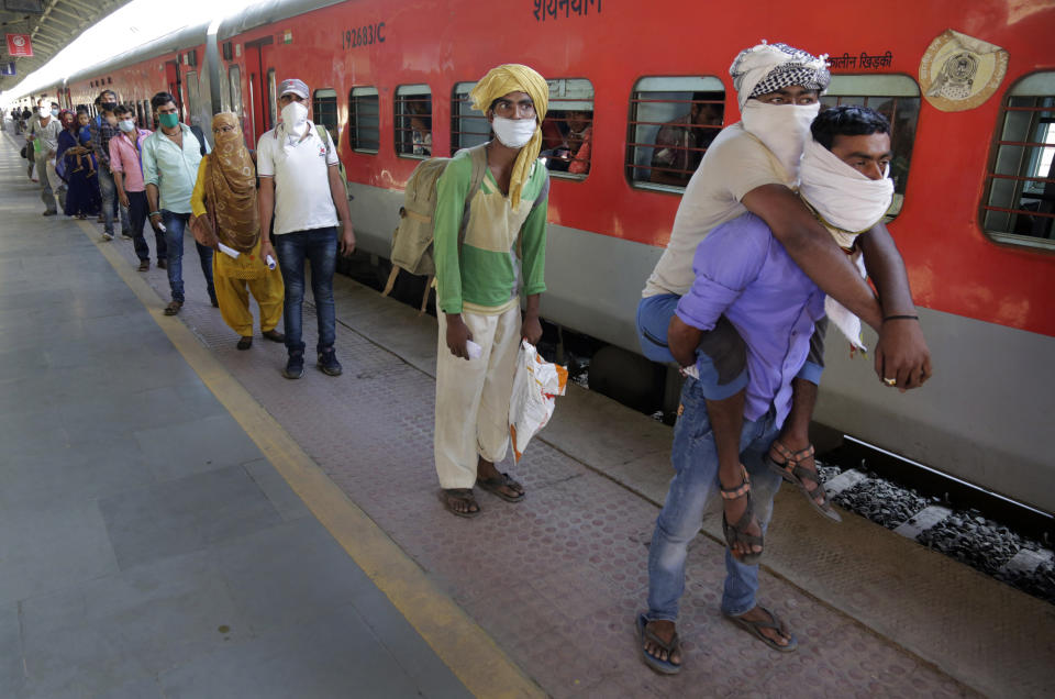 In this Saturday, May 2, 2020, photo, Hira Ali carries his physically disabled brother Muslim Ali on his back as they wait to board a special train to return to Agra in Uttar Pradesh state, during a nationwide lockdown to curb the spread of new coronavirus, at a railway station in Ahmedabad, in the western Indian state of Gujarat. Tens of thousands of impoverished migrant workers are on the move across India, walking on highways and railway tracks or riding trucks, buses and crowded trains in blazing heat. They say they have been forced to leave cities and towns where they had toiled for years building homes and roads after they were abandoned by their employers _ casualties of lockdown to stop the virus from spreading. (AP Photo/Ajit Solanki)