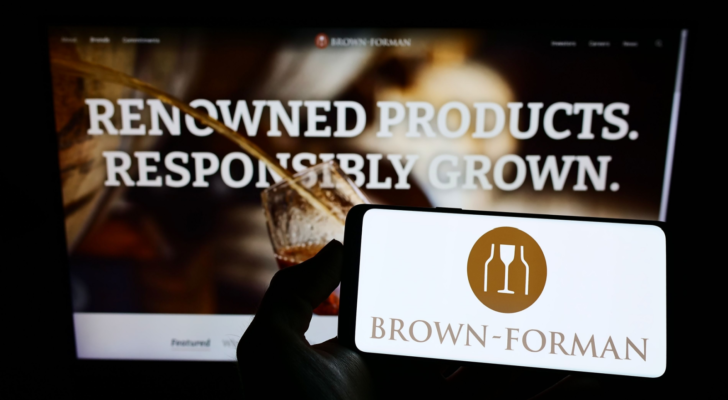 Person holding cellphone with logo of American spirits company Brown-Forman (BF-B) Corporation on screen in front of webpage. Focus on phone display. Unmodified photo.