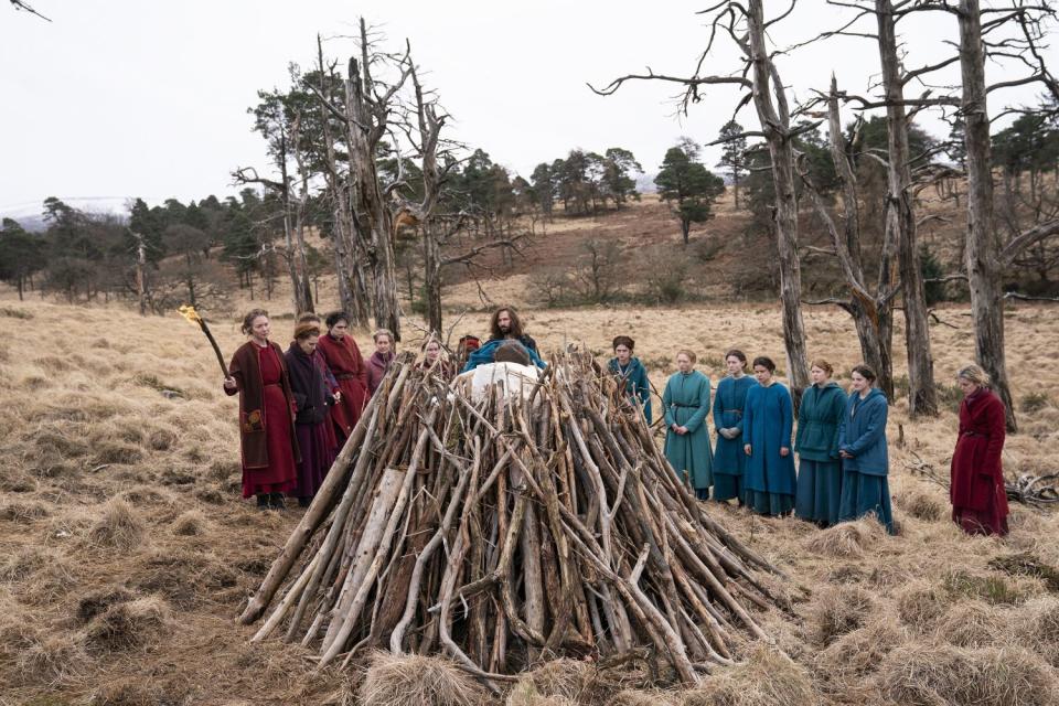 A man and a group of women, one holding a torch, apparently ready to burn another person on a pile of wood.