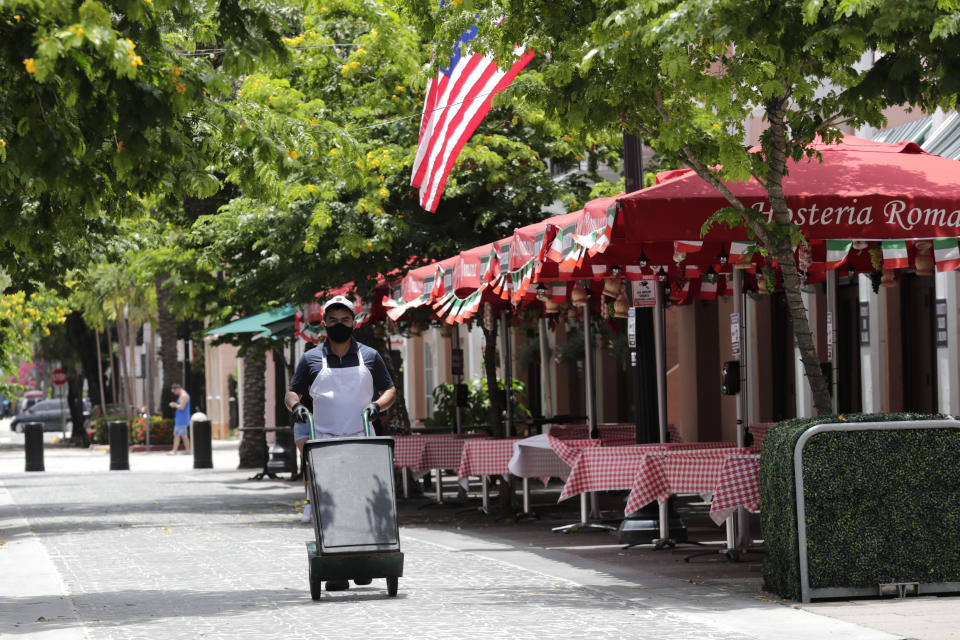 A worker walks past empty tables at the Hosteria Romana restaurant, which is closed to customers, during the coronavirus pandemic, Sunday, July 12, 2020, in Miami Beach, Fla. Restaurants throughout Miami-Dade County are open only for outdoor dining, take-out and delivery. (AP Photo/Lynne Sladky)