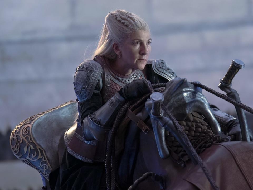 A woman with long silvery-blonde hair wearing armor sits in a saddle.