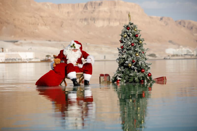 Issa Kassissieh, wearing a Santa Claus costume, looks on as he poses for a picture while sitting next to a Christmas tree on a salt formation in the Dead Sea, near Ein Bokeq