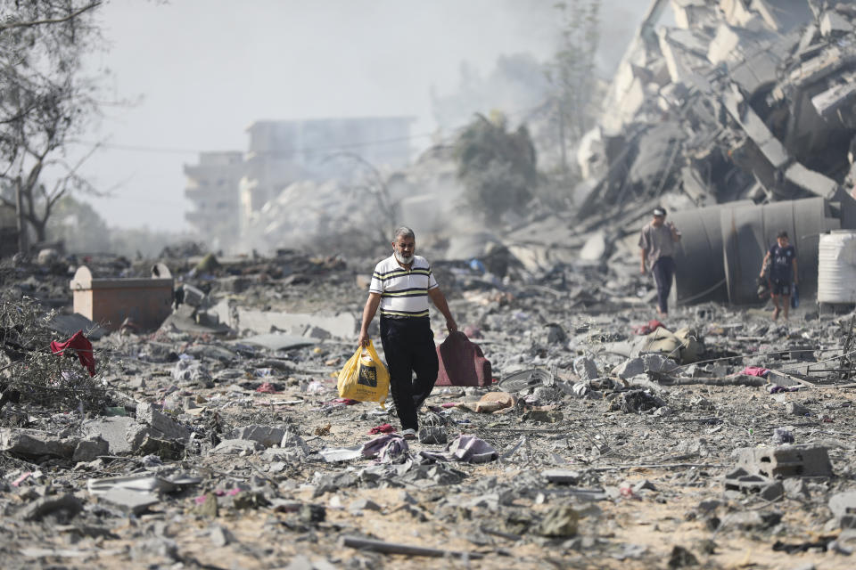 Palestinos caminan el viernes 20 de octubre de 2023 junto a edificios destruidos en un bombardeo israelí sobre al-Zahra, en las afueras de la Ciudad de Gaza. (AP Foto/Ali Mahmoud)