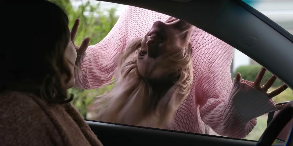 A woman, upside, smiles at another woman in a car