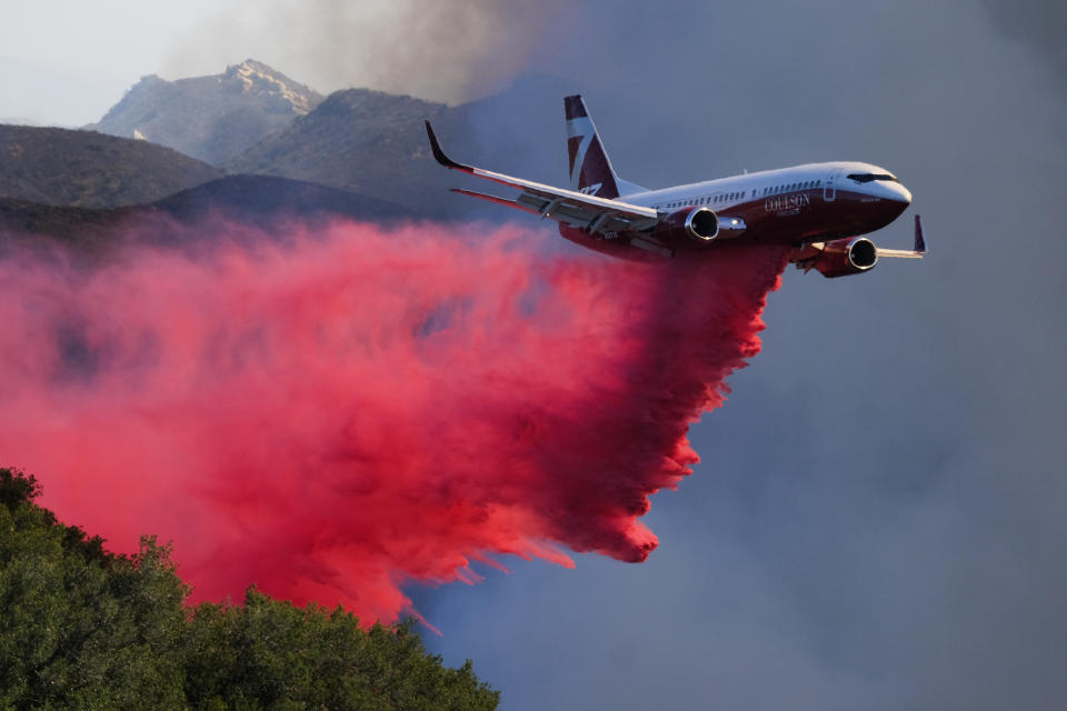 An air tanker drops retardant on a wildfire Wednesday, Oct. 13, 2021, in Goleta, Calif. A wildfire raging through Southern California coastal mountains threatened ranches and rural homes and kept a major highway shut down Wednesday as the fire-scarred state faced a new round of dry winds that raise risk of flames. The Alisal Fire covered more than 22 square miles (57 square kilometers) in the Santa Ynez Mountains west of Santa Barbara. (AP Photo/Ringo H.W. Chiu)