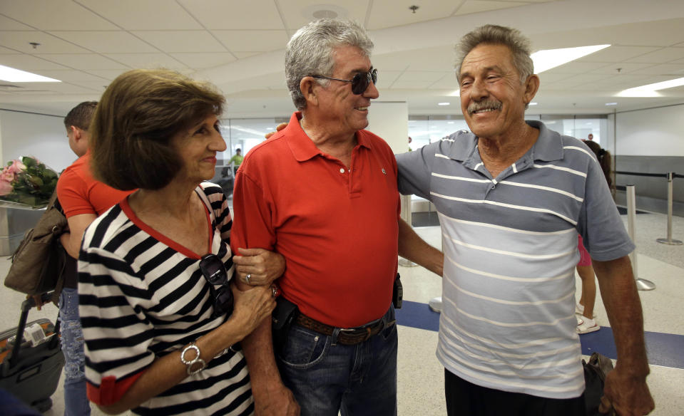 In this Sept. 11, 2013, photo, Benito Perez, right, smiles as he talks to his friends Rogelia Ventura, left, and Luis Ventura, center, at his arrival at Miami International Airport, in Miami. Perez, who had never been on a plane, is one of thousands of Cubans traveling under new laws making travel slightly easier. (AP Photo/Alan Diaz)