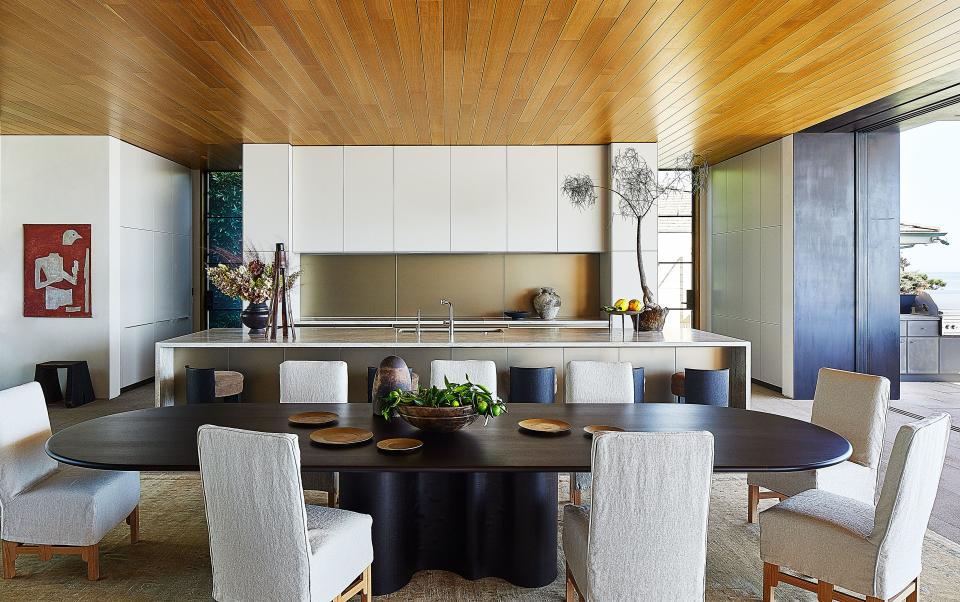 Next to the open-plan kitchen, Axel Vervoordt chairs in a de La Cuona linen slipcovers surround a dining table by Joseph Dirand. Bulthaup kitchen design with Dornbracht fittings; French 1950's painting.