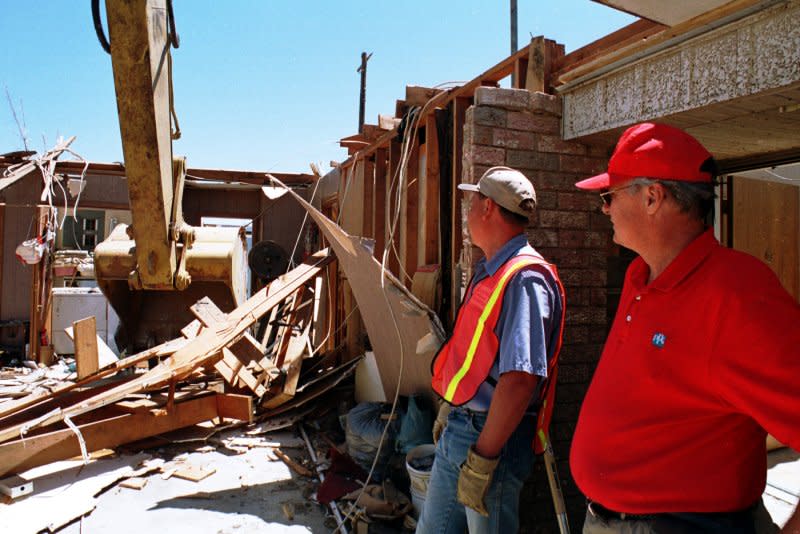 Mark Chase (R) and Jeff Morrison watch as a backhoe takes down the remains of Morrison's father's home in Moore, Okla., on May 7, 1999, four days after a tornado outbreak killed 50 people. File Photo by Ian Halperin/UPI
