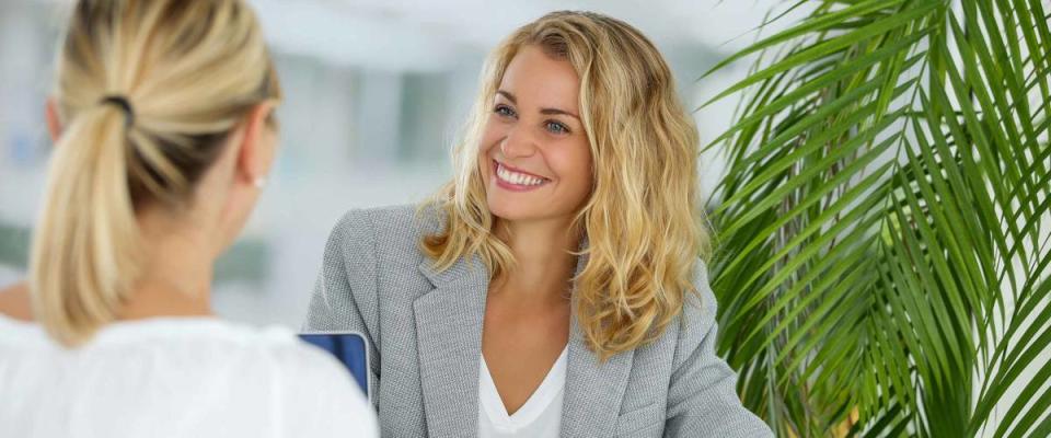 Two women sitting across from each other at a desk, smiling