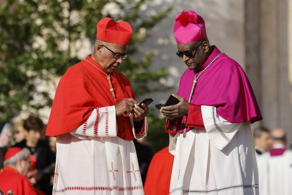 A cardinal, left, and a bishop check their smartphone in St. Peter's Square at The Vatican, Saturday, Sept. 30, 2023, as they wait for a consistory where Pope Francis will create 21 new cardinals to start. (AP Photo/Riccardo De Luca)