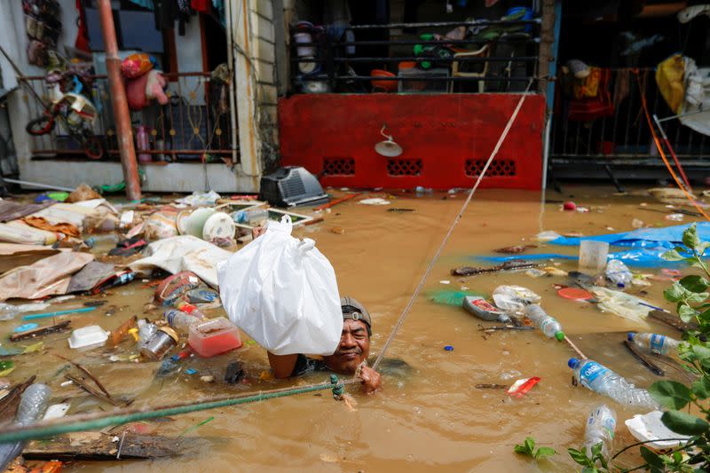 A man hangs on a rope as he distributes food at an area affected by floods after heavy rains in Jakarta