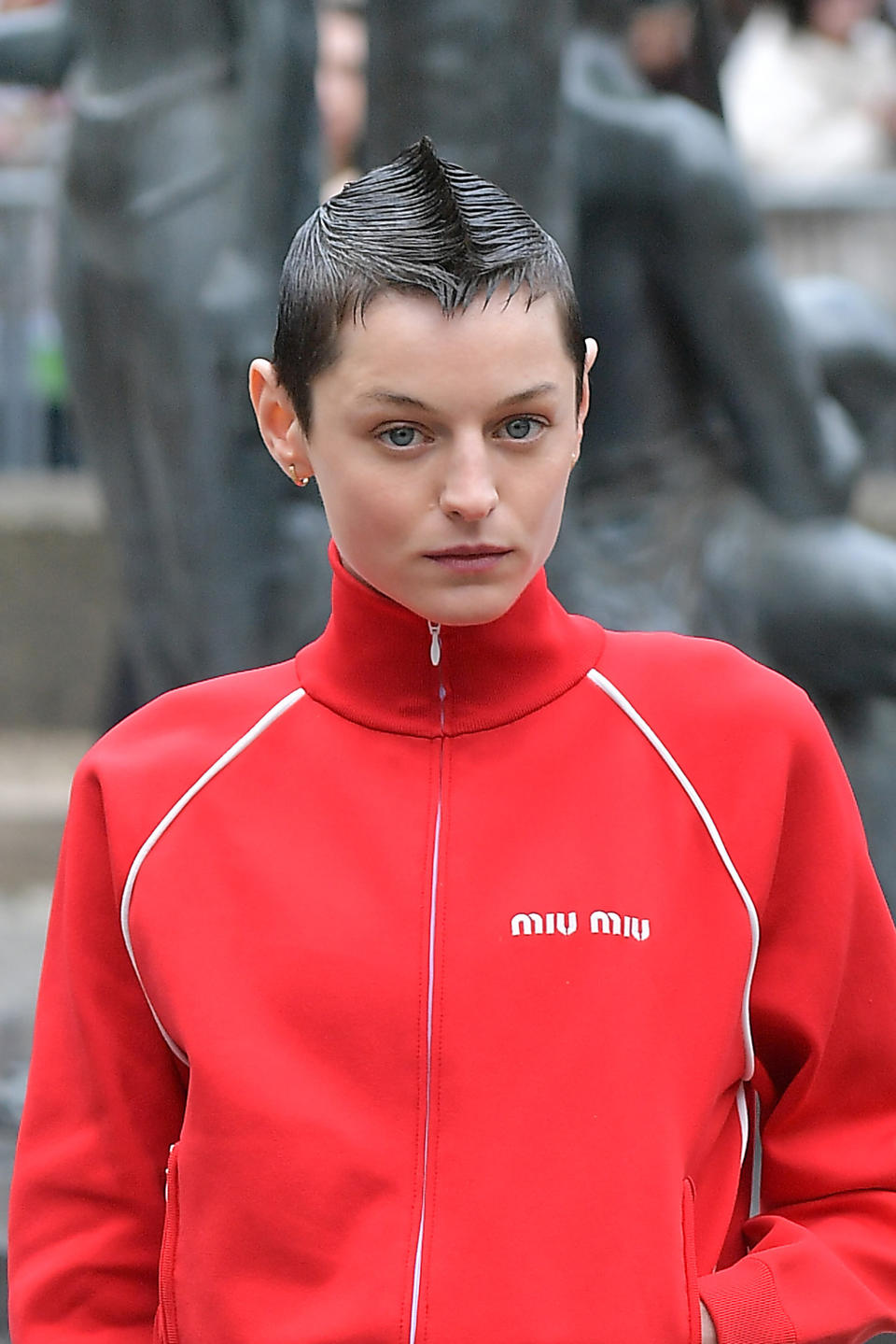 Emma Corrin in a sporty high-neck jacket with a distinctive mohawk hairstyle at a public event