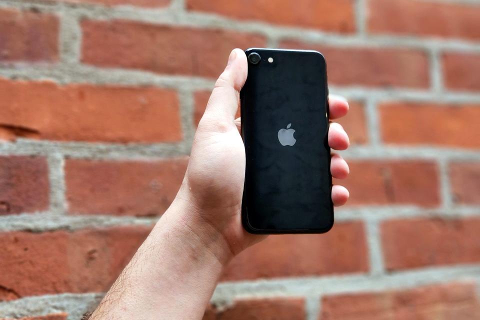 hand holding black iphone se against a brick wall