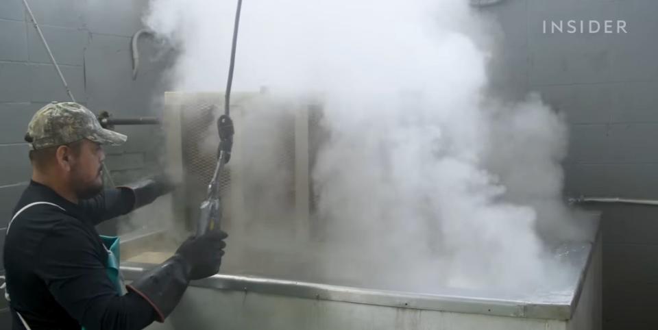 A Parish Seafood Wholesale worker lowering a basket of crawfish into a vat of boiling water.