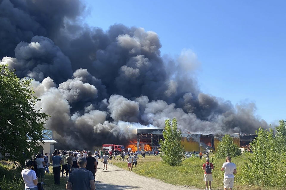 People watch as smoke bellows after a Russian missile strike hit a crowded shopping mall, in Kremenchuk, Ukraine, Monday, June 27, 2022. Ukrainian officials say scores of civilians are feared killed or injured after a Russian missile strike hit a crowded shopping mall in the central city of Kremenchuk. Ukrainian President Volodymyr Zelenskyy said in a Telegram post Monday that the number of victims was 