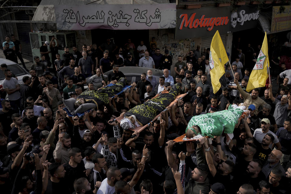 Mourners carry the bodies of three Palestinians draped in the Hamas and Islamic Jihad militant group flags during their funeral in the Jenin refugee camp, West Bank Friday, Nov. 17, 2023. Israeli forces killed the three men in an overnight raid, the Palestinian Health Ministry said Friday. The military wing of the Palestinian Islamic Jihad group claimed the three, including local commander Jamal Lahlouh, 23, as members. (AP Photo/Majdi Mohammed)