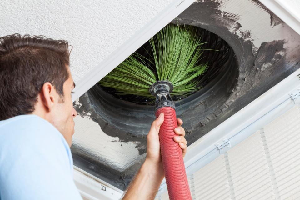 A man cleans a duct in a ceiling.