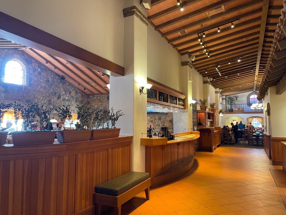 Interior hallway in Olive Garden with wooden paneling and ceiling, a tan tile floor, and plants lining the wall