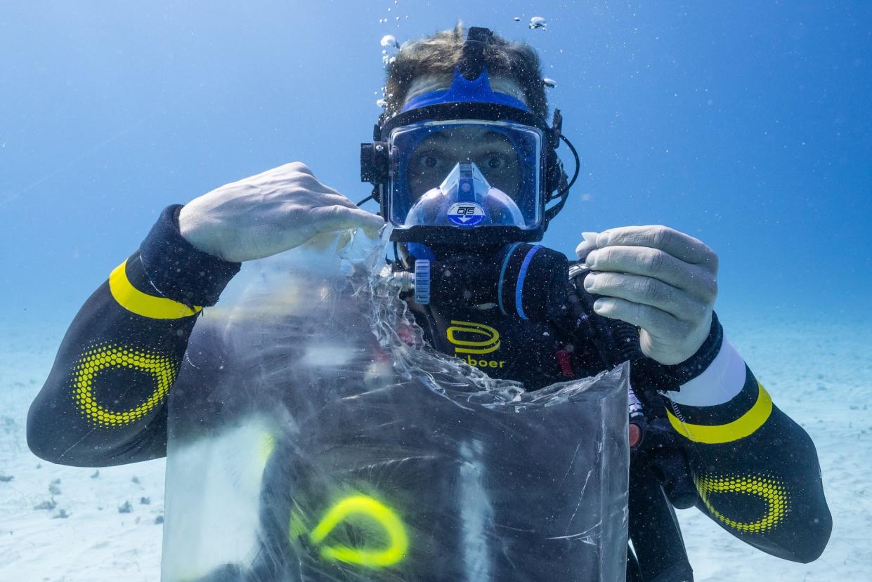 Ross Edgley in scuba gear holding a clear block of gelatin with a shark bite taken out of it