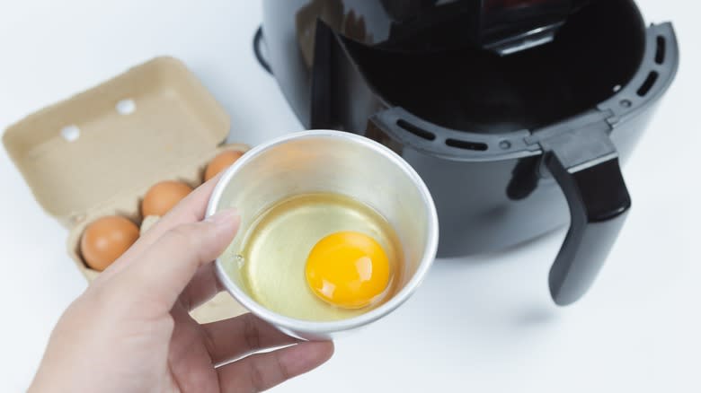 hand holding egg over air fryer