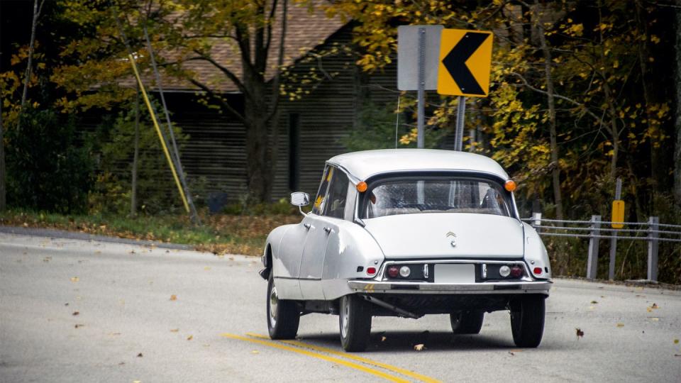 a light grey citroen ds sedan goes through a curve on a leafy road