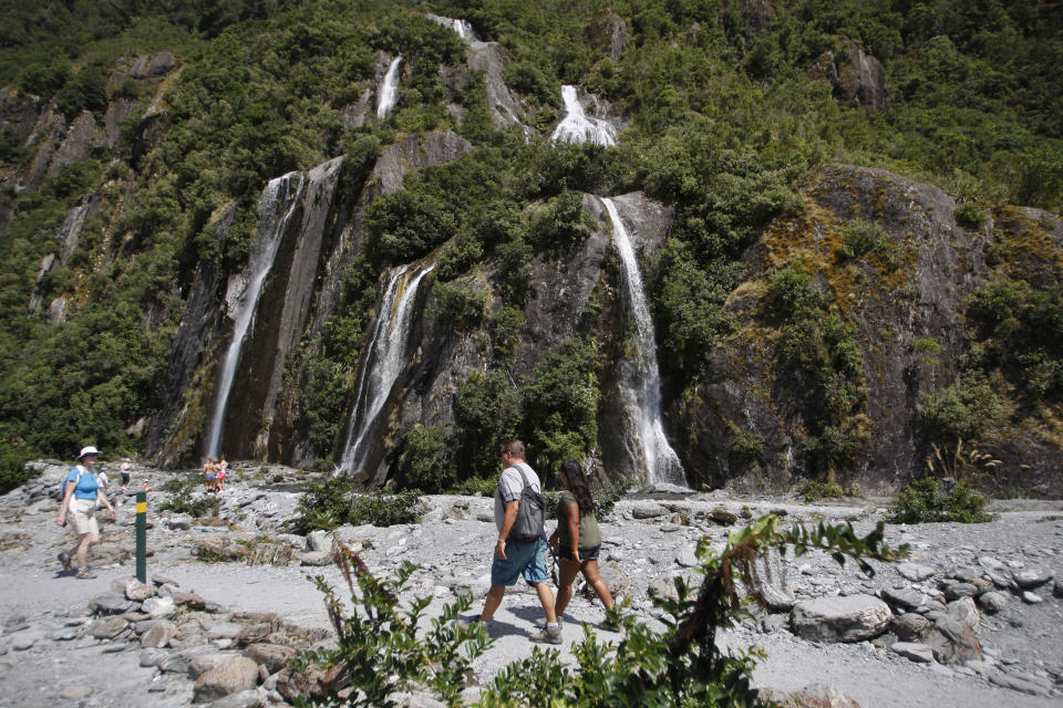 In this Feb. 7, 2016 file photo, tourists walk past waterfalls at the Franz Josef Glacier in New Zealand. The Fox and Franz Josef glaciers have been melting at such a rapid rate that it has become too dangerous for tourists to hike onto them from the valley floor, ending a tradition that dates back a century. (AP Photo/Nick Perry)