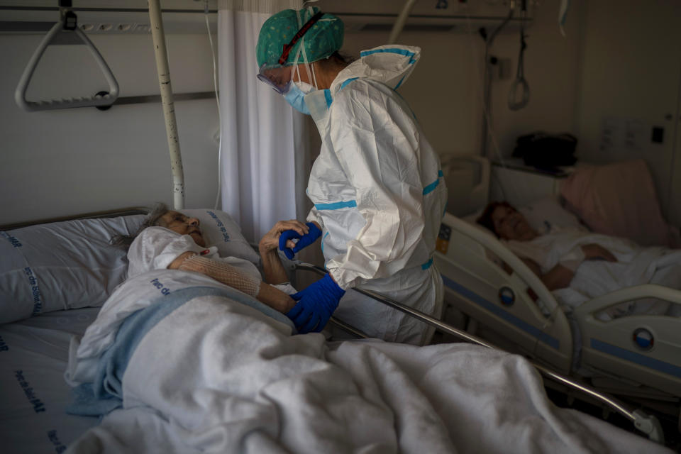 FILE - In this Nov. 18, 2020, file photo, Nurse Marta Fernandez holds the hand of one of her patients, Maria Teresa Argullos, 94, at the hospital del Mar in Barcelona, Spain. "The worst thing about this pandemic is seeing how patients deal alone with the entire disease process, even with their own death," says Fernández. "Seeing them die alone is the hardest of all." (AP Photo/Emilio Morenatti, File)