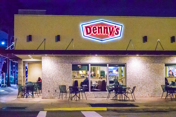 Exterior of a Denny's restaurant at night with illuminated signage and visible indoor diners