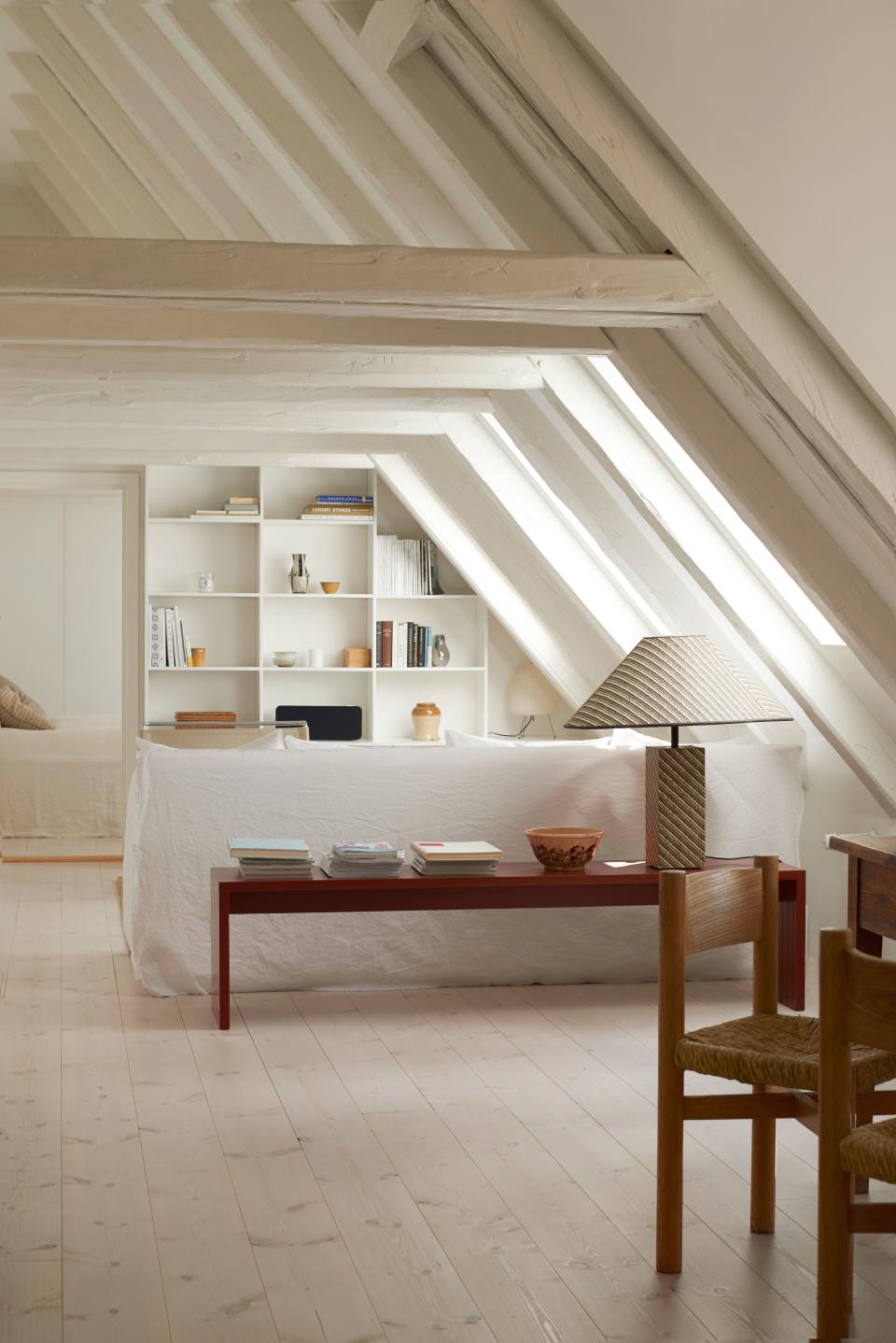 A look into the living room shows the whitewashed, angled wooden beams that create spectacular visual lines (and the need for a custom built-in bookshelf) over the home. A bench the Feiffers also designed sits behind a white linen sofa by Italian Gervasoni, at once a display area and a place to sit if needed. The lamp is a rare woven raffia lamp from the 1980s.