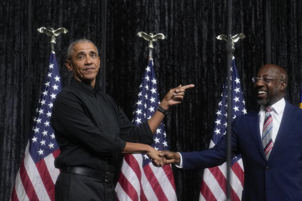 Former President Obama greets Sen. Raphael Warnock in front of American flags.