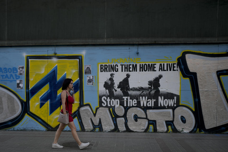 A woman walks in front of an anti-war poster in Kyiv, Ukraine, Friday, June 10, 2022. With war raging on fronts to the east and south, the summer of 2022 is proving bitter for the Ukrainian capital, Kyiv. The sun shines but sadness and grim determination reign. (AP Photo/Natacha Pisarenko)