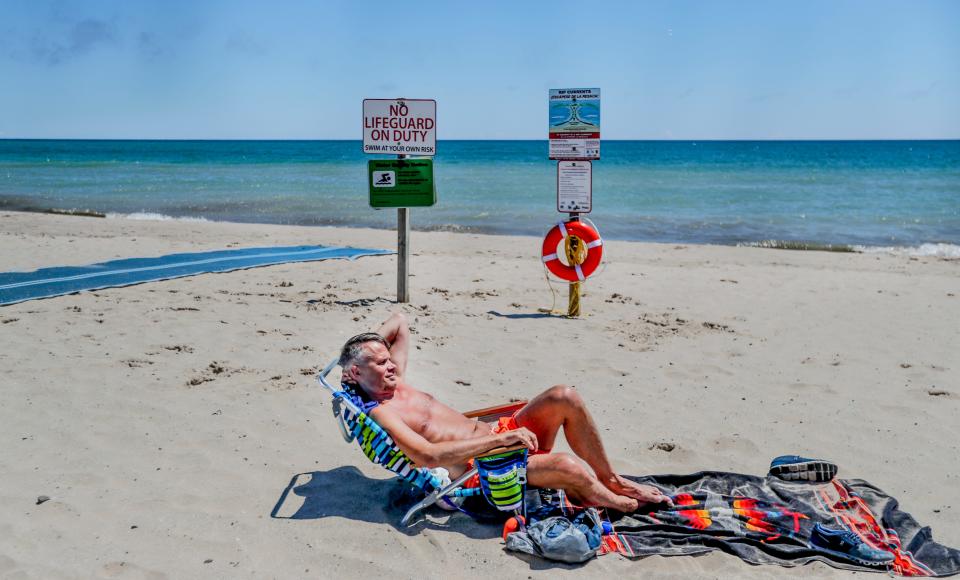 A beachgoer who didn't want to be identified sunbathes in front of a "No Lifeguard on Duty" sign July 1, 2021, at Bradford Beach in Milwaukee.