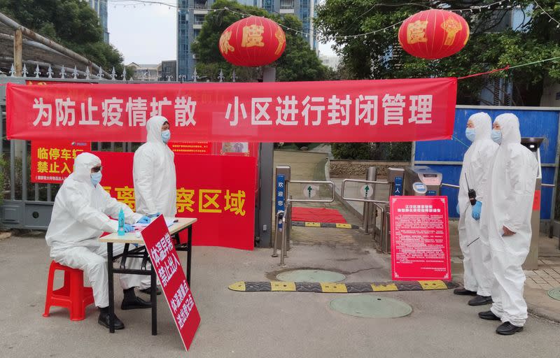 Workers in protective suits are seen at a checkpoint for registration and body temperature measurement, at an entrance to a residential compound in Wuhan