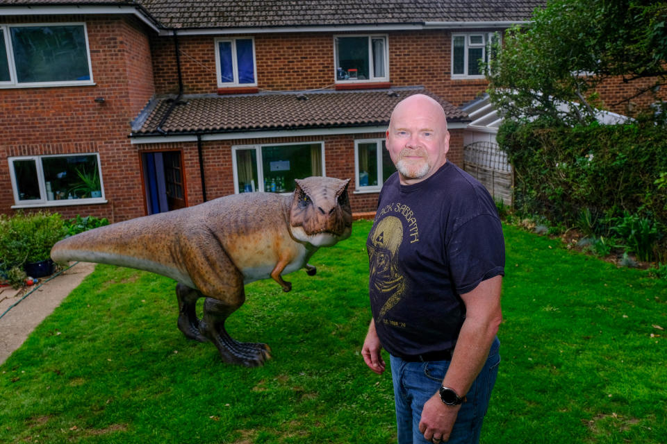 A wacky husband shocked his wife who wanted to brighten up their garden with a gnome - by installing a 12ft-tall replica of a T-REX on the patio. Adrian Shaw, 52, snapped up the 14-stone resin and fiberglass dinosaur and hired a crane to winch it into position on Thursday (3/9). He came up with the madcap-scheme after wife Deborah, 53, begged him to clean up the back garden of their home in Leamington Spa, Warks. The IT analyst paid £1,600 for the replica of the terrifying beast, which he named ‘Dave’ and put it on the patio.