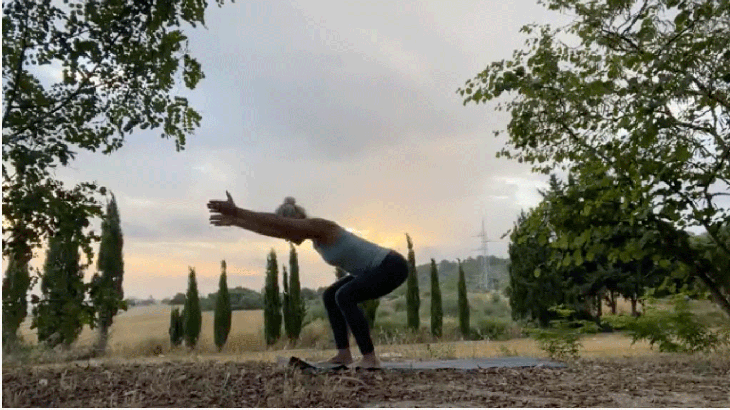 Woman practicing yoga outside with her knees bent and her arms alongside her ears