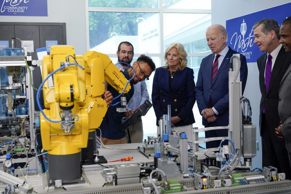 President Joe Biden listens as Bryce Lewis, Industrial Systems Student at Nash Community College, demonstrates how a yellow robot arm can move during a visit to Nash Community College in Rocky Mount, N.C., Friday, June 9, 2023. First lady Jill Biden, North Carolina Gov. Roy Cooper and Rep. Don Davis, D-N.C., look on. (AP Photo/Susan Walsh)