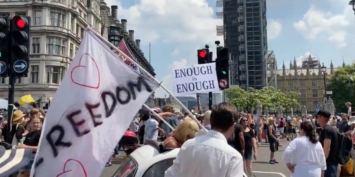 A video still showing people holding signs and flags that say 'enough is enough' and 'freedom'