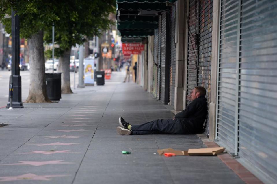 A man sits in front of a row of shuttered shops along Hollywood Boulevard in LA.