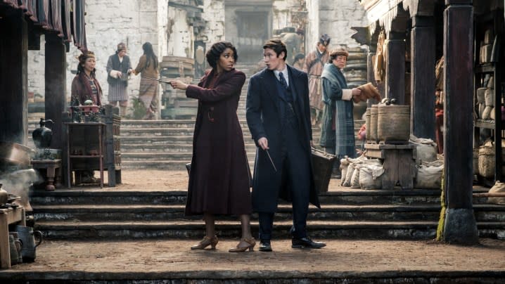 Jessica Williams and Callum Turner stand back-to-back in a street in Fantastic Beasts 3.