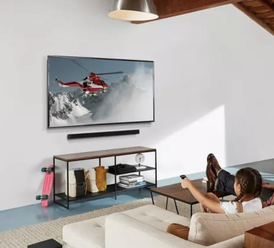 A child pointing a remote at a television with a sound bar underneath it