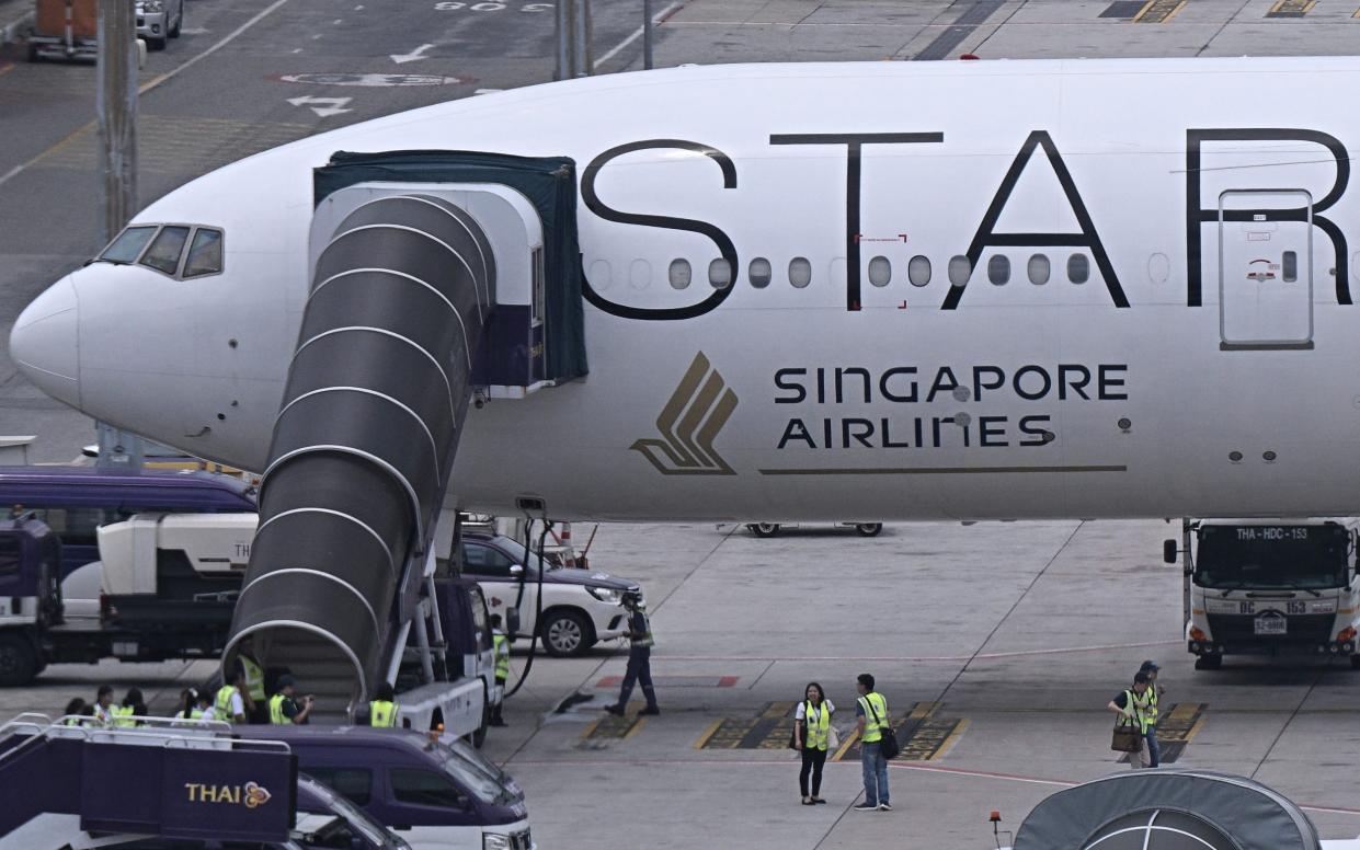 The jet has a set of covered stairs attached to its bow doors. People stand around in hi-vis vests