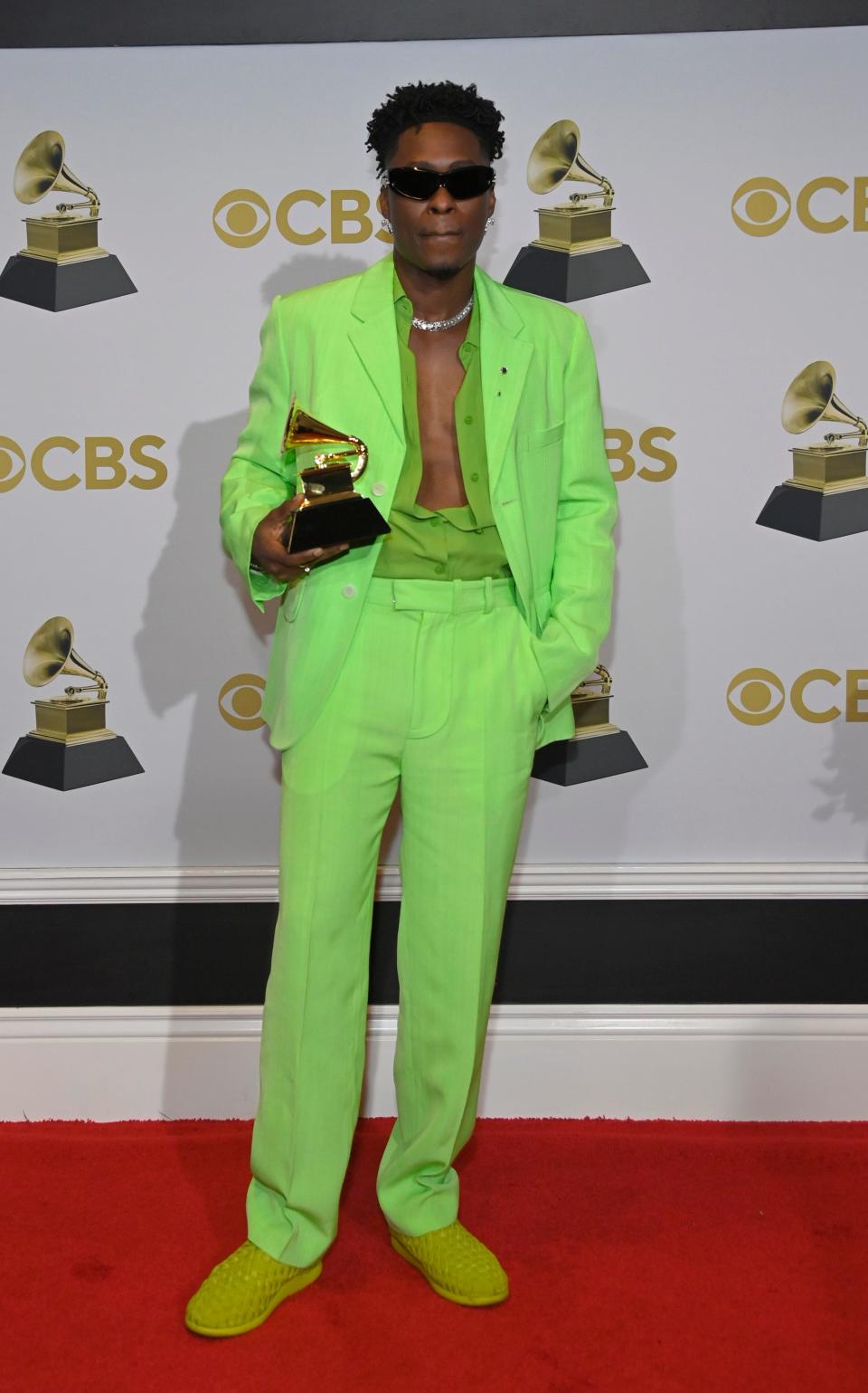 Lucky in a neon green blazer and pants with a matching unbuttoned top. He's wearing woven lime green shoes.