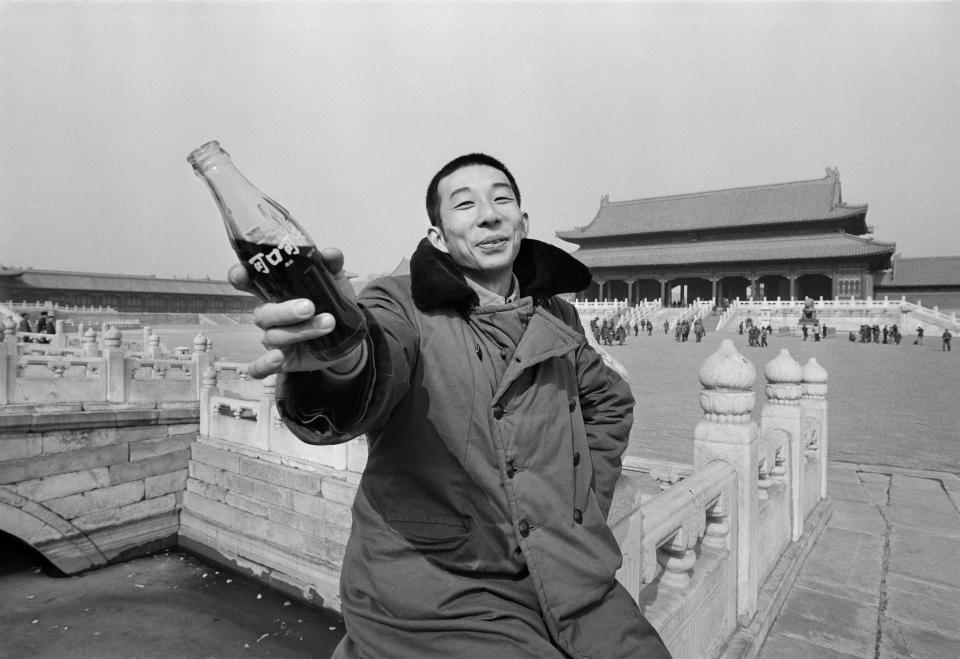 A young man holds a glass bottle of Coca-Cola, which had just resumed production in China, outside the Forbidden City, Beijing, 1981. | Liu Heung Shing