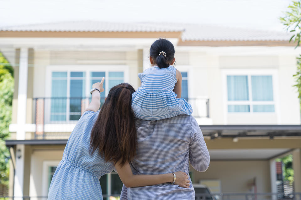 Back view of happy family moving into new house admiring their house.