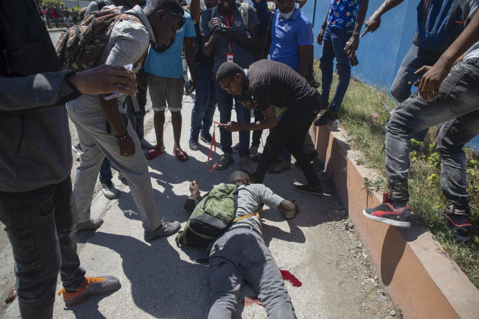 People stand around a man who was injured by gunfire during a protest by factory workers demanding higher salaries in Port-au-Prince, Haiti, Wednesday, Feb. 23, 2022. Men wearing police uniforms fired into the group after thousands of factory workers launched a new strike to demand higher wages than those the prime minister announced earlier this week. (AP Photo/Odelyn Joseph)