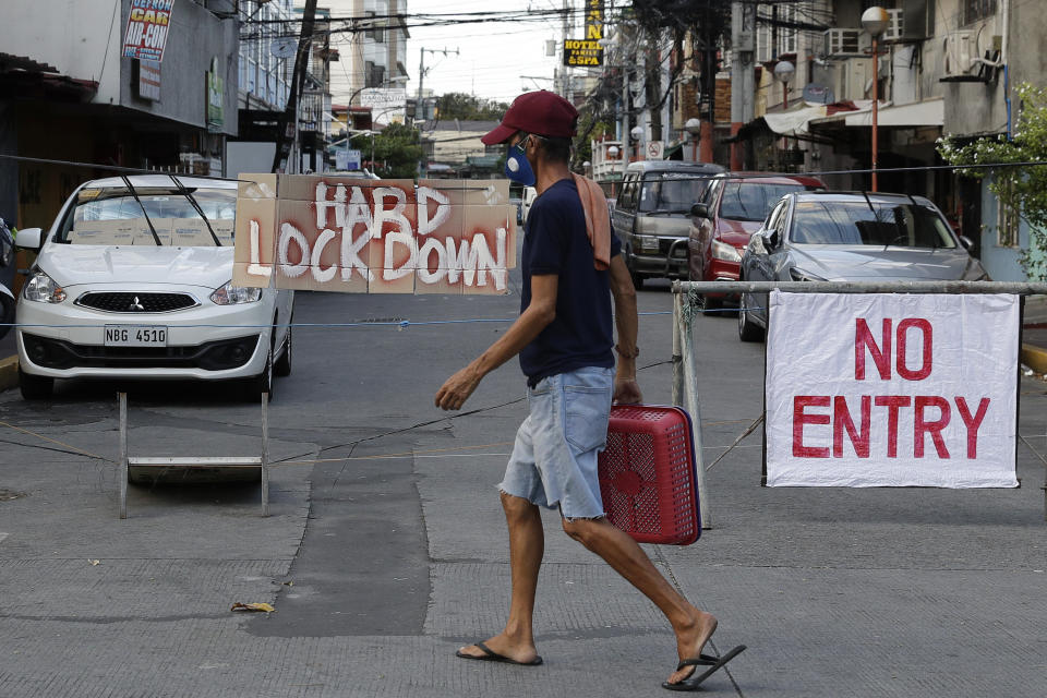 A man wearing a protective mask passes by a sign placed in the middle of a road during a stricter community quarantine to prevent the spread of the new coronavirus in Manila, Philippines, Friday, April 24, 2020. Philippine President Rodrigo Duterte angrily threatened to declare martial law after accusing communist rebels of killing two soldiers who were escorting food and cash deliveries during a coronavirus quarantine. (AP Photo/Aaron Favila)