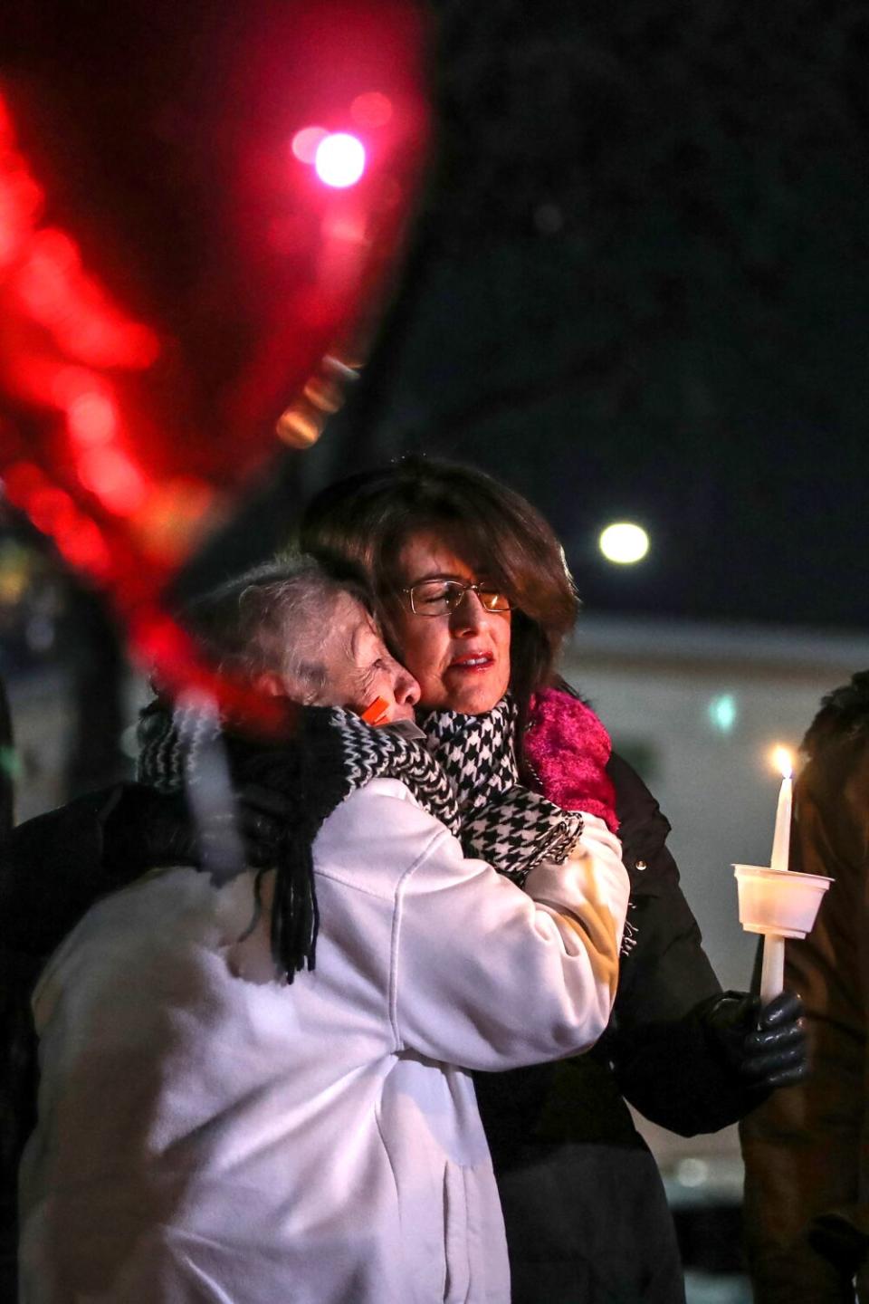 Two people embrace while one holds a lit thin candle.