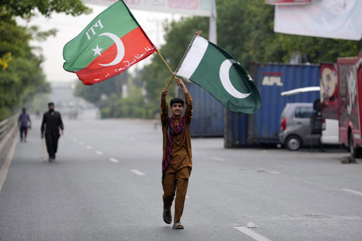 A supporter of Pakistan's former Prime Minister Imran Khan holds flags near his house, in Lahore, Pakistan, Wednesday, May 17, 2023. Police surrounded the home of Pakistan's former Prime Minister Khan on Wednesday, claiming he was sheltering dozens of people allegedly involved in violent protests over his recent detention. (AP Photo/K.M. Chaudary)