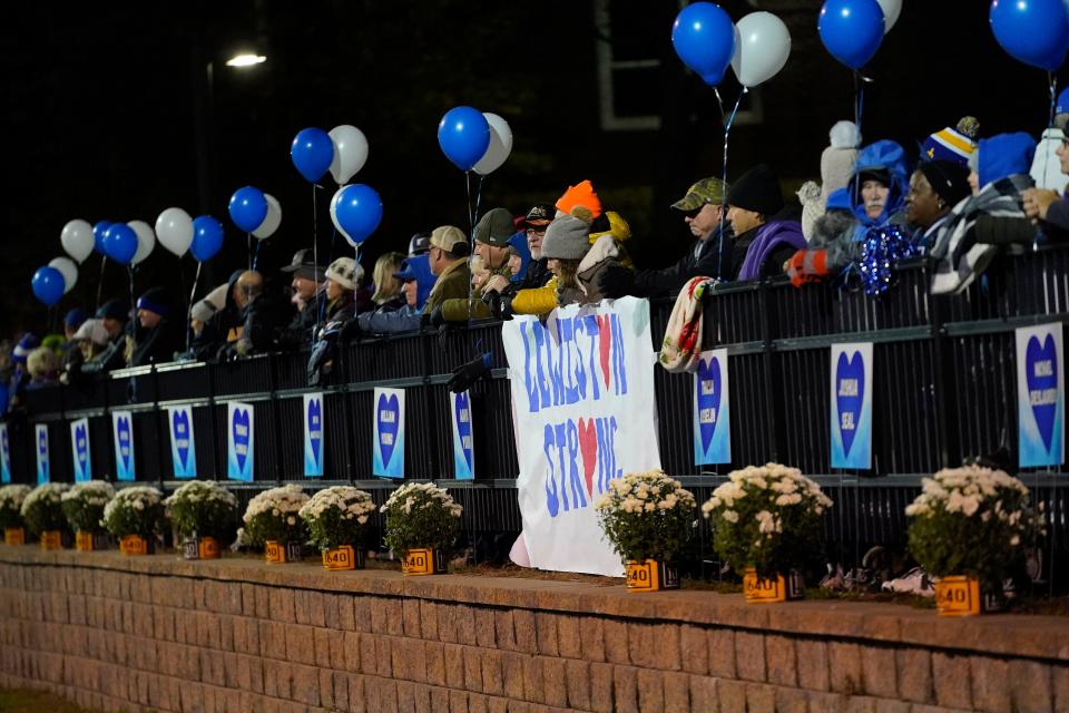 The names of the Lewiston shooting victims hang from the fence near fans during a football game between Lewiston High School and Edward Little High School, Wednesday, Nov. 1, 2023, in Lewiston, Maine. Locals seek a return to normalcy after the mass shooting on Oct. 25. (AP Photo/Matt York)